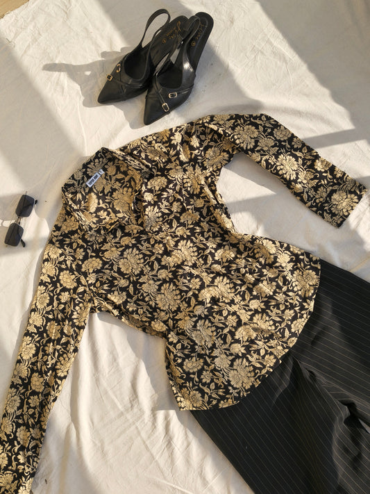 Black and gold floral shirt on a white sheet with black high heels and sunglasses.